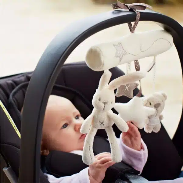Peluche blanche animale avec sonnette suspendue avec un bébé qui regarde la peluche
