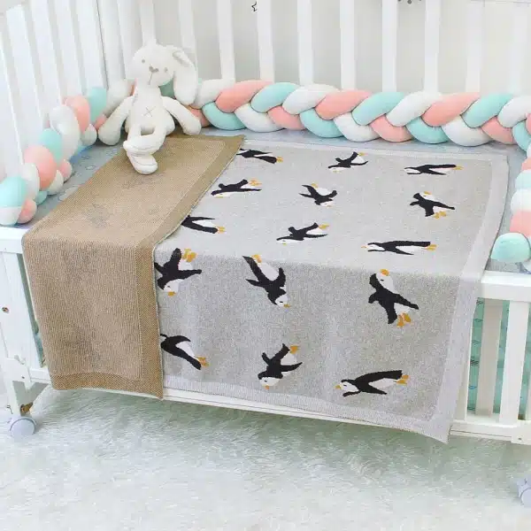 Une couverture tricotée en motif pingouin dans un lit de bébé avec plusieurs peluches