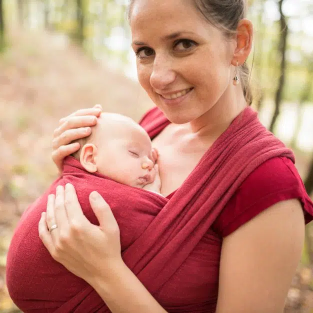 maman qui porte son bébé avec un porte bébé ergonomique dans la forêt