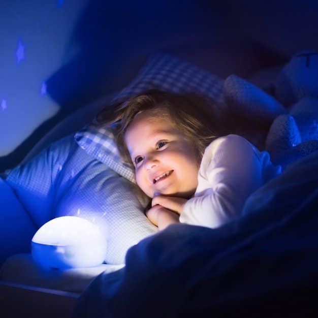 fille qui écoute l'histoire que sa maman lui raconte avant de dormir à côté d'une veilleuse avec une lumière bleue