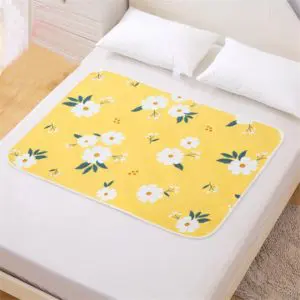 Couche réutilisable pour bébé à fleur coloris jaune et blanc sur un lit blanc