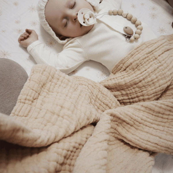 Couverture pour bébé en mousseline biologique beige avec un bébé qui dort