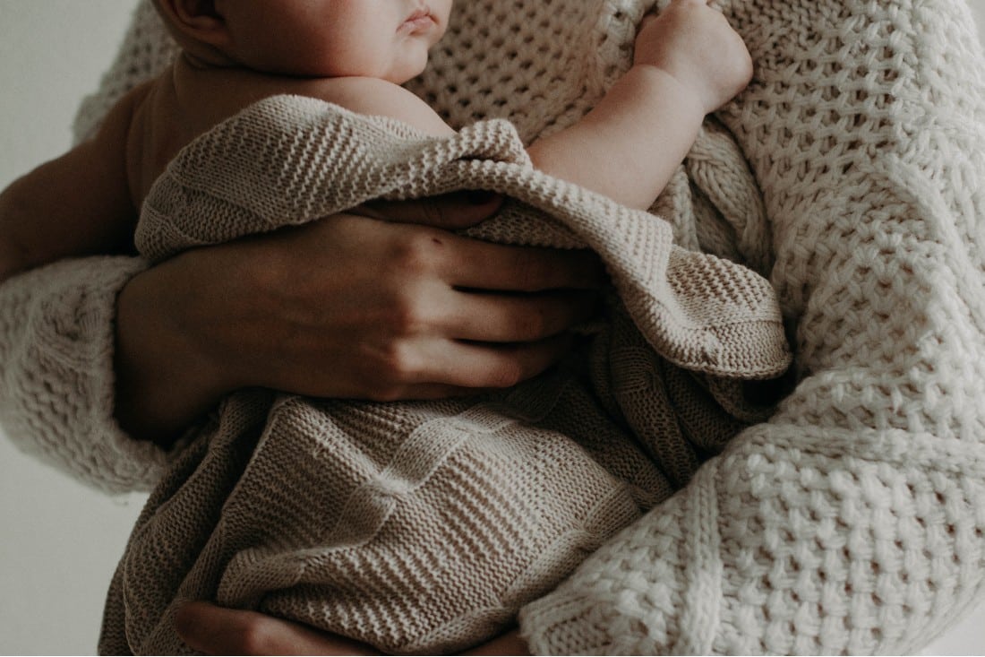 bébé dans les bras de sa maman enroulé dans une couverture 
