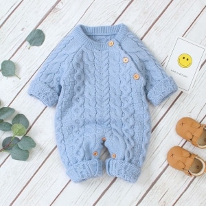 Barboteuse tricotée à manches longues pour bébé bleu avec un fond en bois et des petites chaussures marron sur le côté