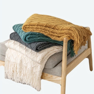 Couverture avec glands tricotés pour nouveau-né avec plusieurs coloris différents sur un fauteuil