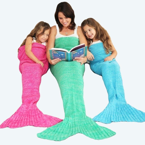 Une maman dans le lit avec ces deux filles qui sont avec la couverture en forme de sirène une rose une bleue et une verte