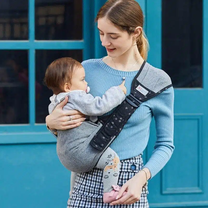 Porte bébé en écharpe. Le porte bébé qui permet de tenir votre enfant par devant. L'enfant est assis dans le porte bébé. Une grosse écharpe permet de sécuriser l'attache par dessus l'épaule.