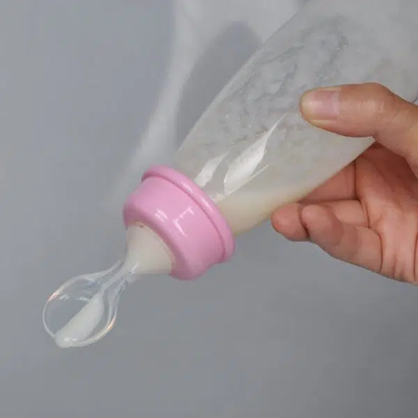 Biberon de sécurité pour bébé rose transparent avec un fond gris et une main qui tient le biberon