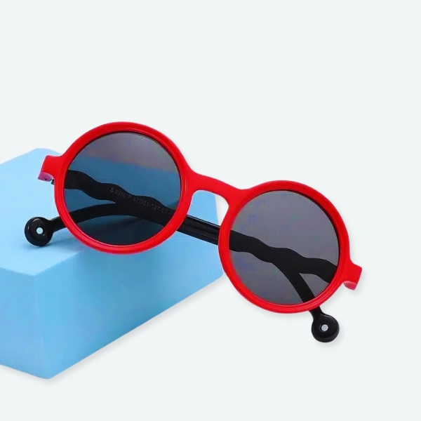 Lunette de soleil ronde pour enfants de couleur rouge avec les lentilles noires et un fond avec un cube bleu