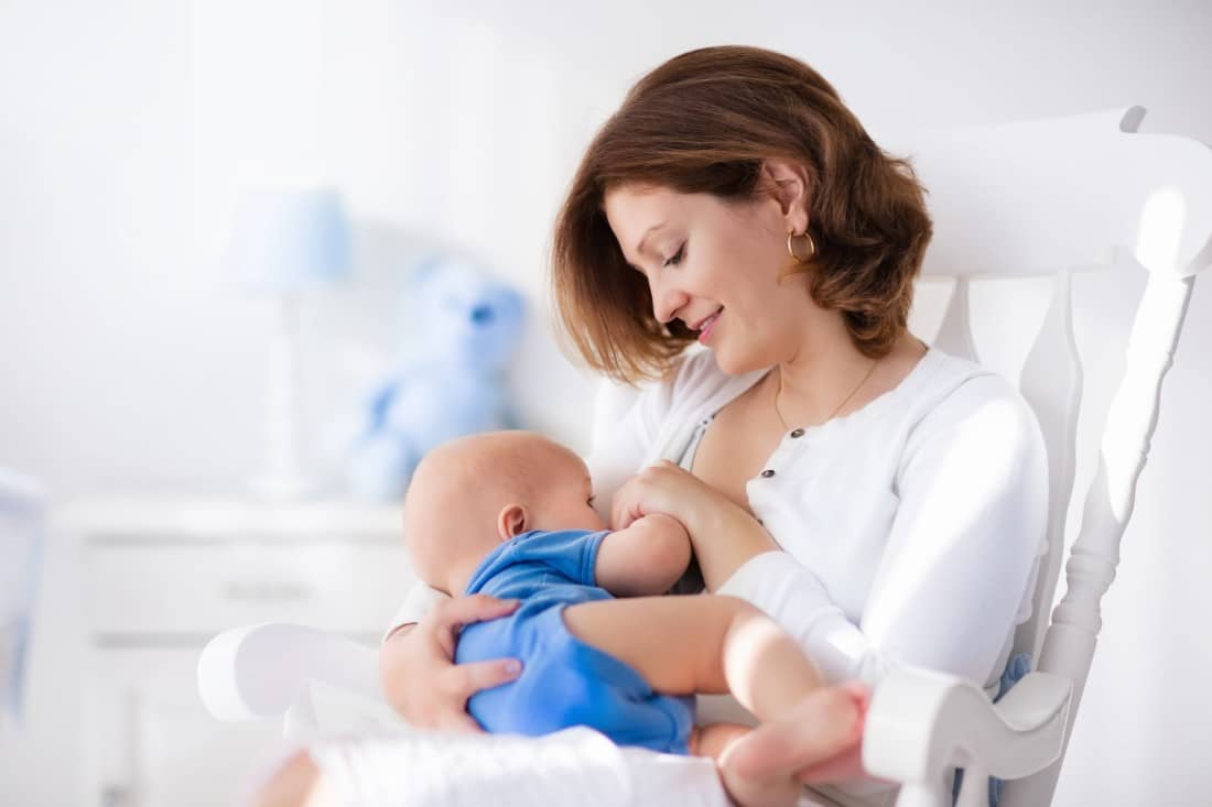 une jeune maman assise dans une chaise qui allaite son bébé et qui se demande "Comment savoir si bébé mange assez ?"