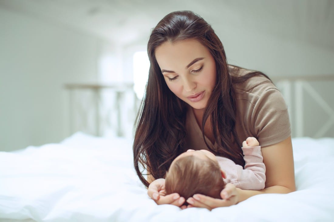 une jeune maman qui enlace son bébé sur son lit