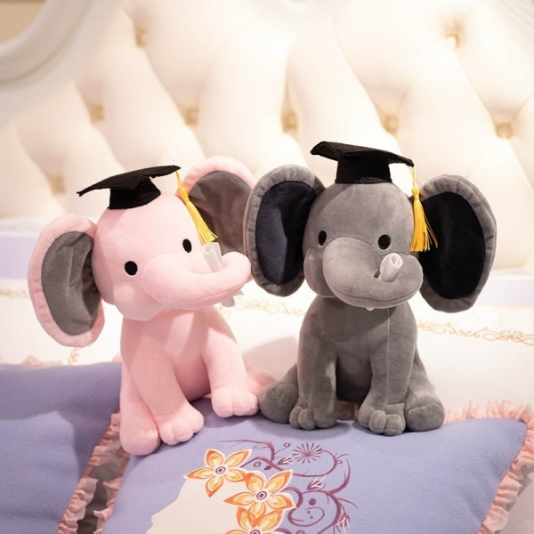 Deux peluches en forme d'éléphant un rose et un gris avec un chapeau d'étudiant sur le lit