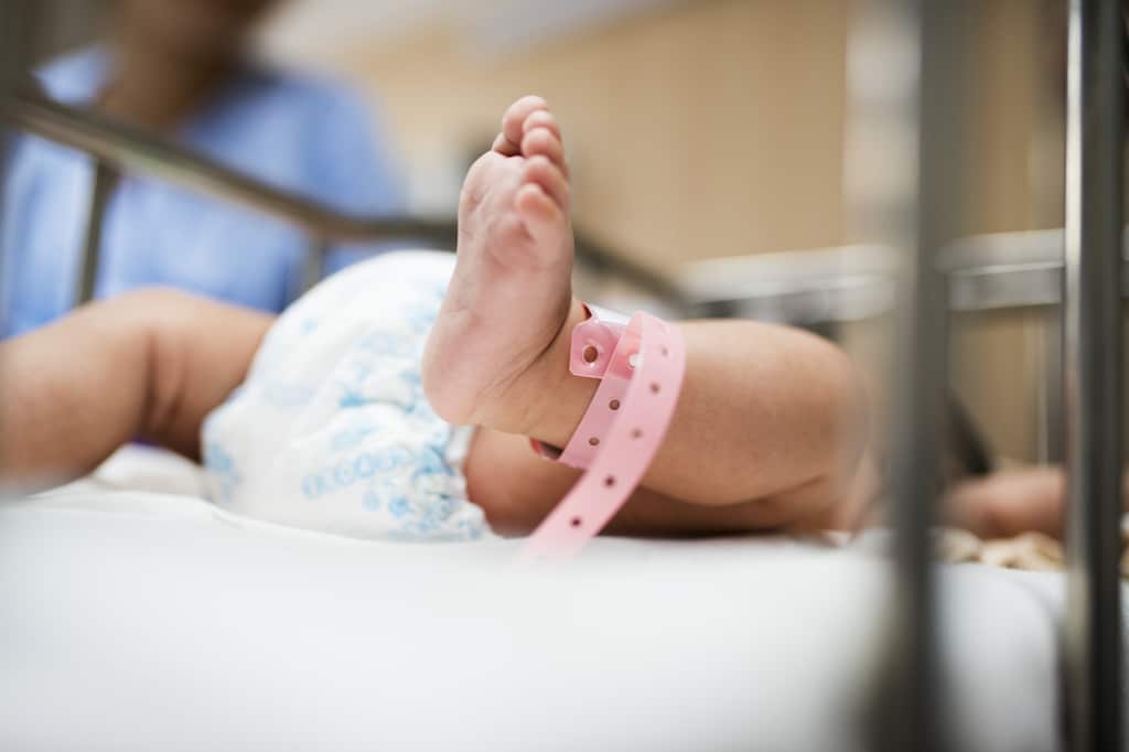 un bébé est allongé dans son berceau à l'hopital avec une vue ses jambes et le bracelet enroulé autour de sa cheville