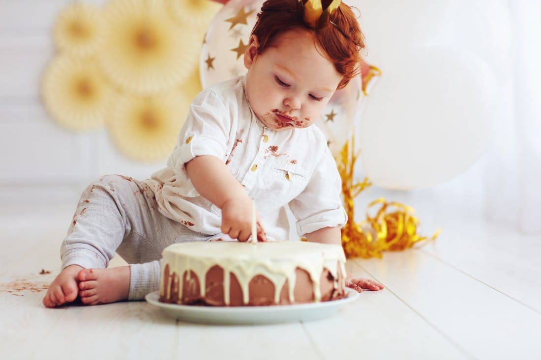 bébé assis devant son gâteau d’anniversaire avec du chocolat autour de sa bouche  