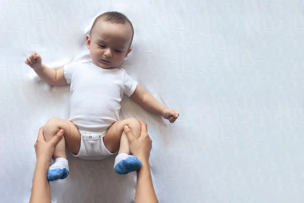 un bébé est allongé avec les jambes repliées par 2 mains qui effectuent un massage pour aider bébé à faire caca