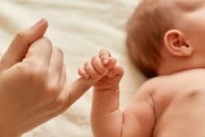 un bébé allongé tient le petit doigt d'une main d'adulte