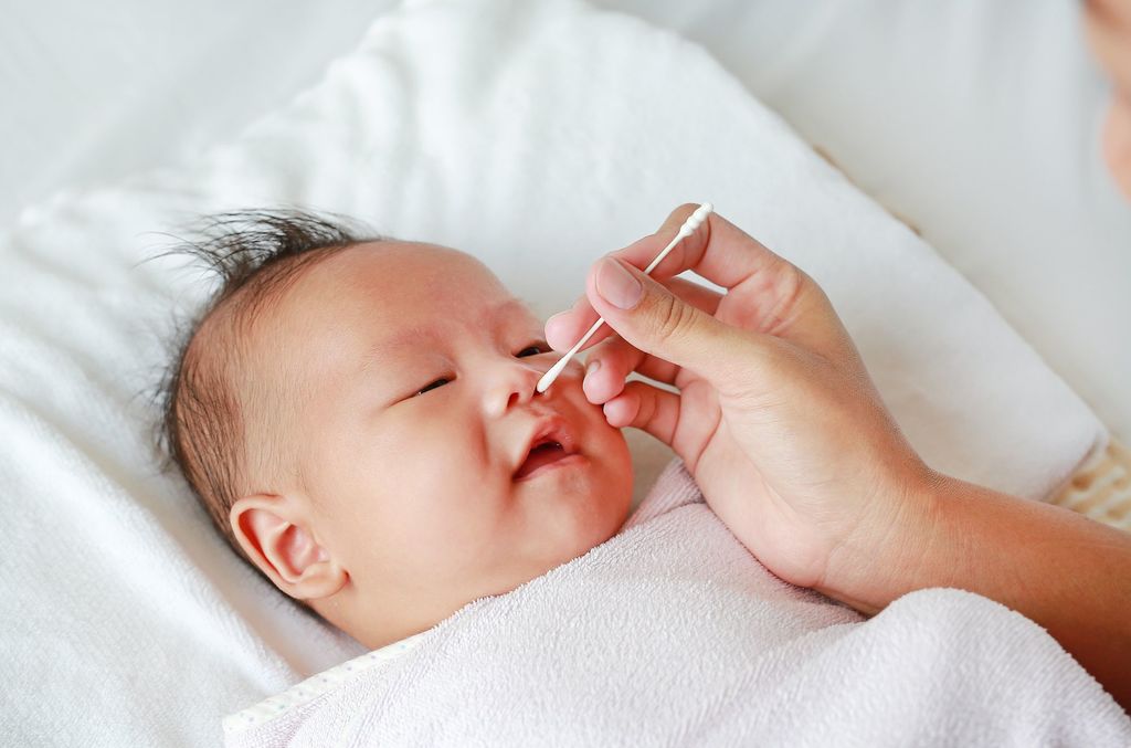 une main tient un coton-tige et le passe sur les narines d'un bébé allongé