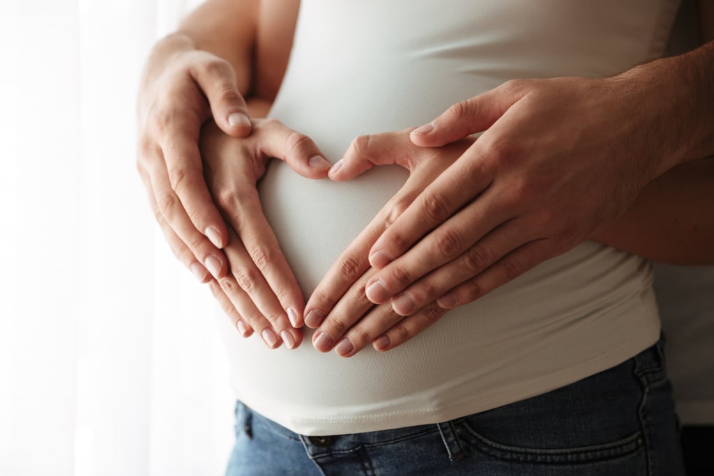 Portrait rapproché d'un homme et d'une femme faisant le signe du coeur avec leurs mains sur le ventre arrondi de la femme enceinte. Difficile d'encore savoir quand sent on bébé bouger, il n'en fait encore qu'à sa tête dès que papa pose sa main