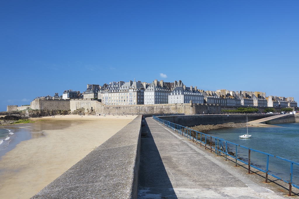 vue des remparts de la ville de saint malo depuis la promenade avec la plage sur la gauche et un petit voilier sur la droite