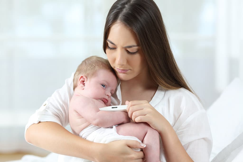une maman tient son bébé dans les bras avec un thermomètre