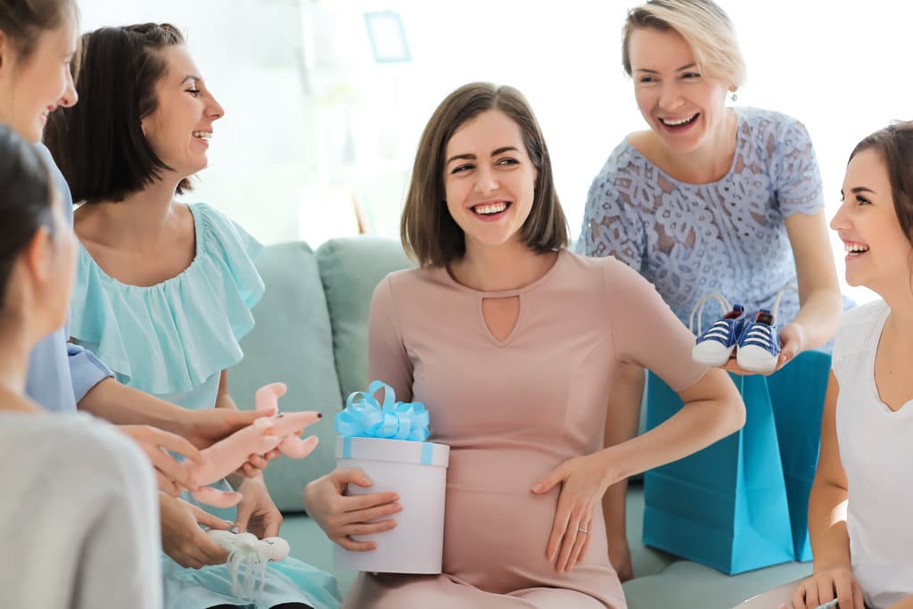 une femme enceinte assise est entourée d'autres femmes qui lui offrent des présents. elles sont toutes souriantes et enjouées.