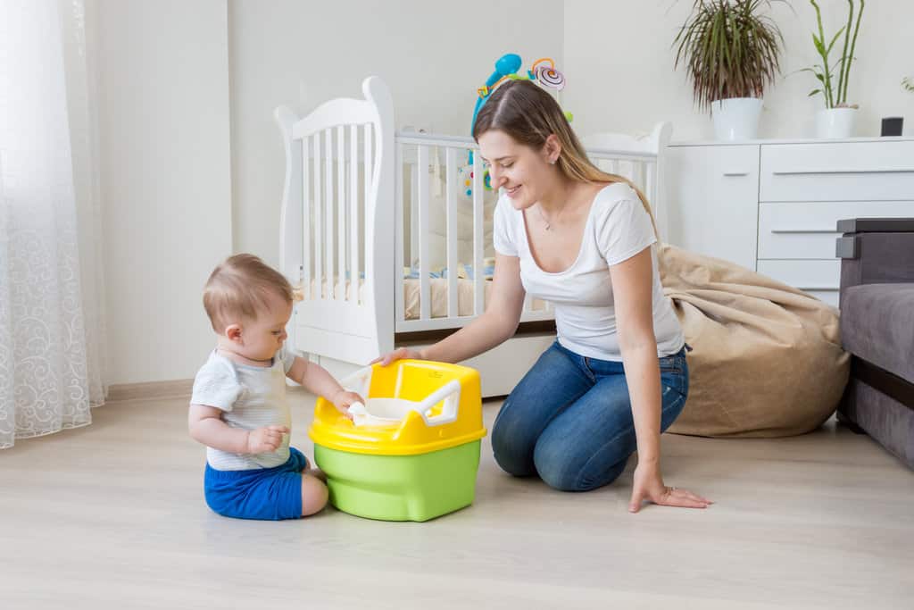 dans le salon, un bébé assis par-terre appréhende et touche un pot jaune et vert, aux côtés de sa maman