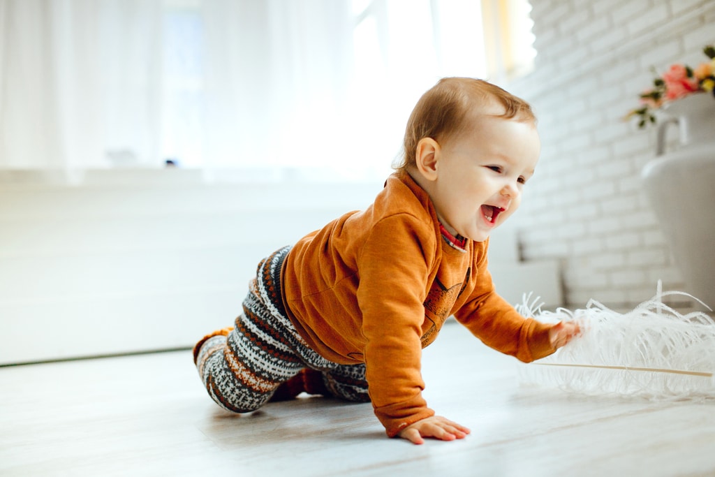 un bébé heureux à quatre pattes, se déplace dans la maison avec un jouet qu'il touche.