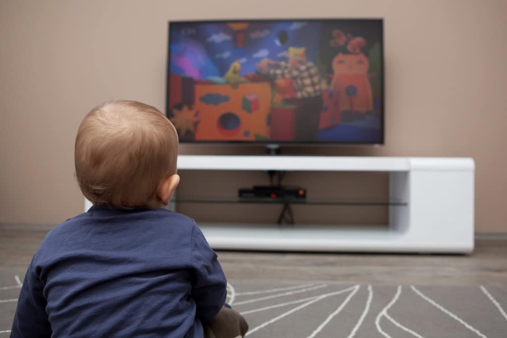 un bébé est assis parterre dans le salon et regarde des dessins-animés sur la télévision
