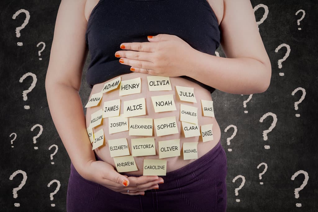 une femme enceinte montre son ventre rond sur lequel sont collés des post-it jaunes avec des prénoms dessus