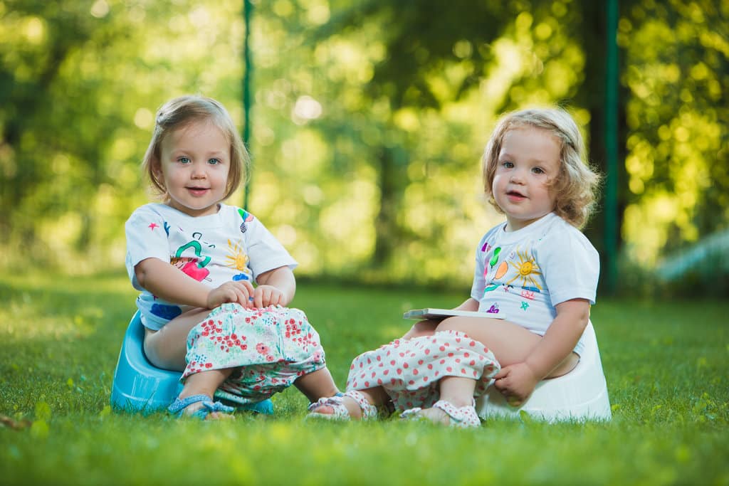 deux petites filles sont assises sur le pot dans un parc. elles prennent la pose en regardant le photographe.