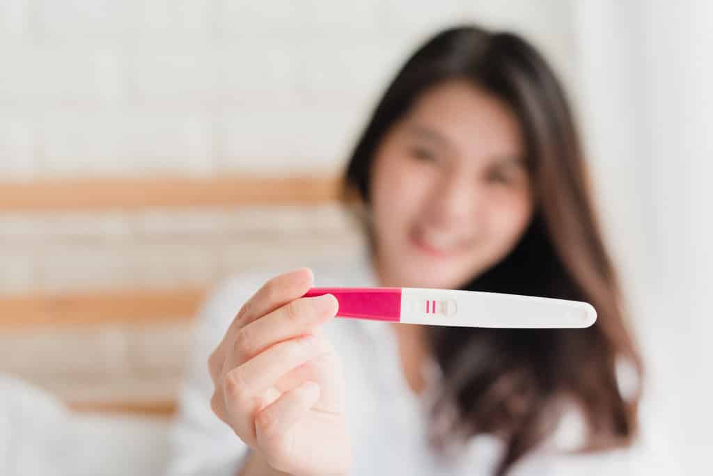 une jeune femme tient un test de grossesse positif rose dans sa main qu'elle met en avant sur la photo