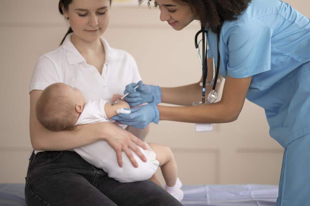 une maman tient son bébé dans ses bras tandis qu'une pédiatre lui administre un vaccin