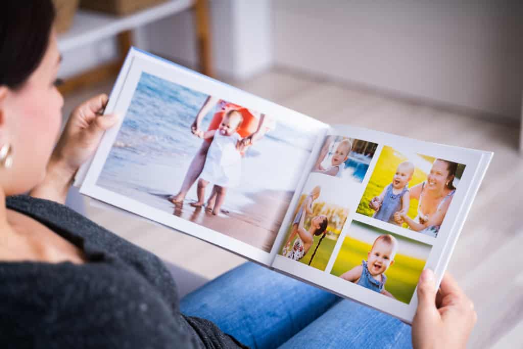 une femme tient dans ses mains un album photo souvenirs grand ouvert qu'elle feuillette assise. Dans l'album, on peut voir des photos d'un bébé avec ses parents.