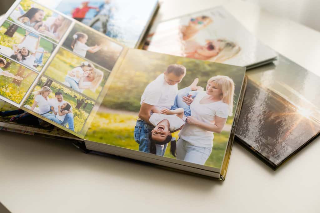 plusieurs albums photo sont posés en vrac sur un table. en premier plan, un album photo est ouvert dans lequel il y a des photos de parents avec leur petit garçon