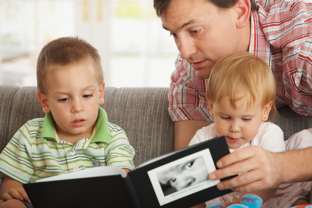 un père montre des albums photo à ses enfants assis sur un canapé