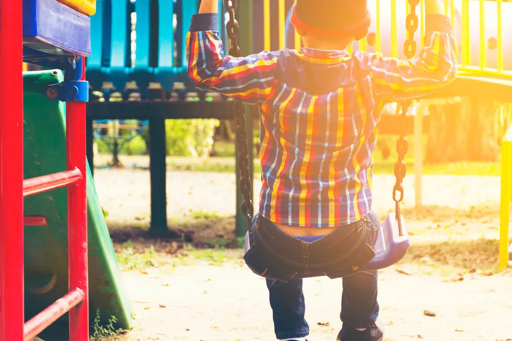un enfant est assis, de dos, sur une balançoire, dans un parc de jeux