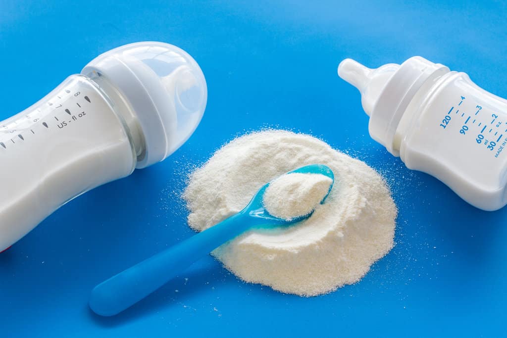 photo de 2 biberons de lait sur fond bleu ainsi que de poudre de lait posé avec une cuillère bleue