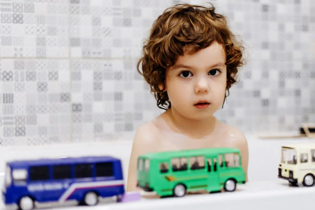 plan rapproché d'un enfant assis dans une baignoire avec devant lui des bus miniatures