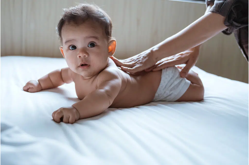 une femme a les mains posées en train de faire un massage à un  bébé sur le ventre qui regarde le photographe