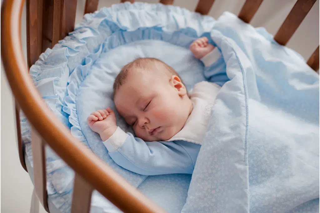 un bébé dort dans un berceau en bois. il est vêtu de bleu et sa literie est également bleue.