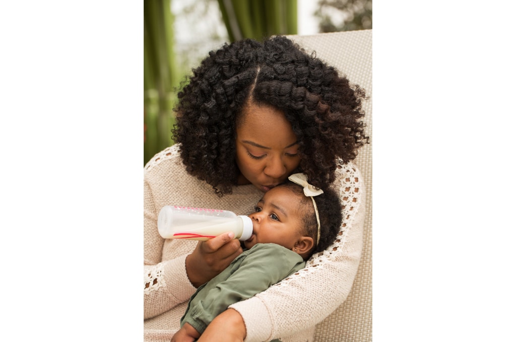 une femme donne le biberon à sa petite fille en lui faisant un bisou sur le front.