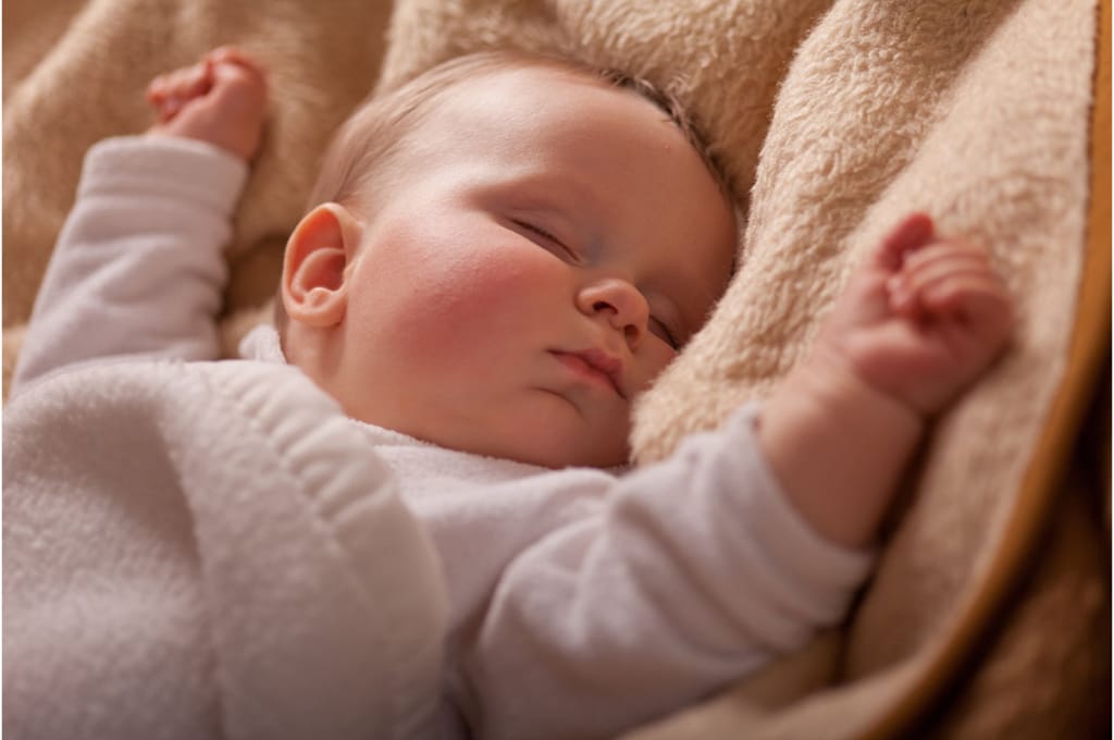 plan rapproché sur un bébé endormi dans une couverture beige. ses joues sont rouges.