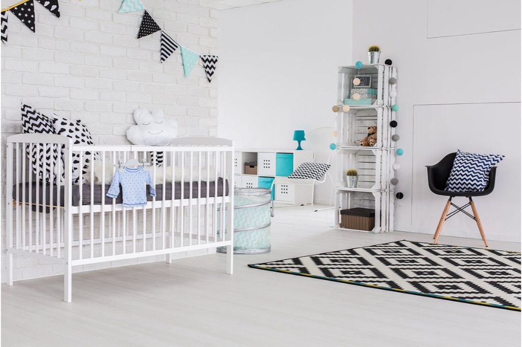 plan d'une chambre de bébé dans le style scandinave. on y voit un lit à barreaux blanc, un tapis, une chaise avec un coussin, une étagère blanche avec des guirlandes dessus et divers objets de décoration.