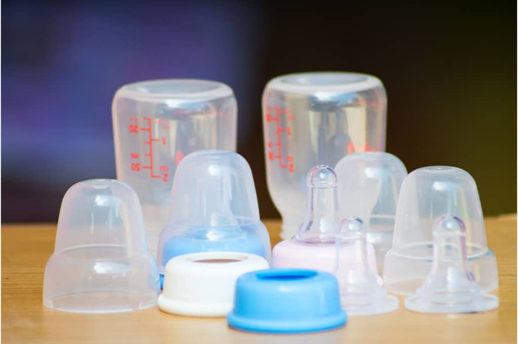 sur une table sont posés 2 biberons en plusieurs pièces désassemblées. les tétines et bouchons sont posés à côté des bouteilles.