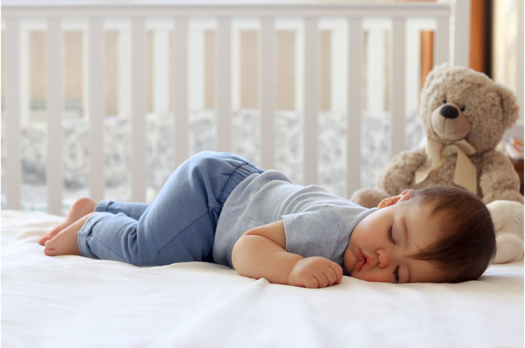 un bébé est endormi sur le ventre sur un lit avec un ours en peluche posé à côté de lui.
