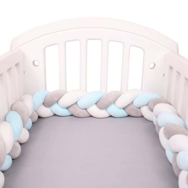Tour de lit tressé blanc gris bleu dans un lit de bébé avec un fond blanc