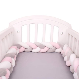 Tour de lit tressé rose blanc gris dans un lit de bébé avec un fond blanc
