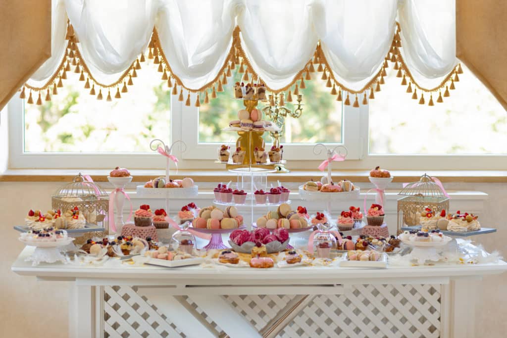sur une table blanche, sont posés pleins de petits gâteaux et macarons disposés dans des plats et assiettes.