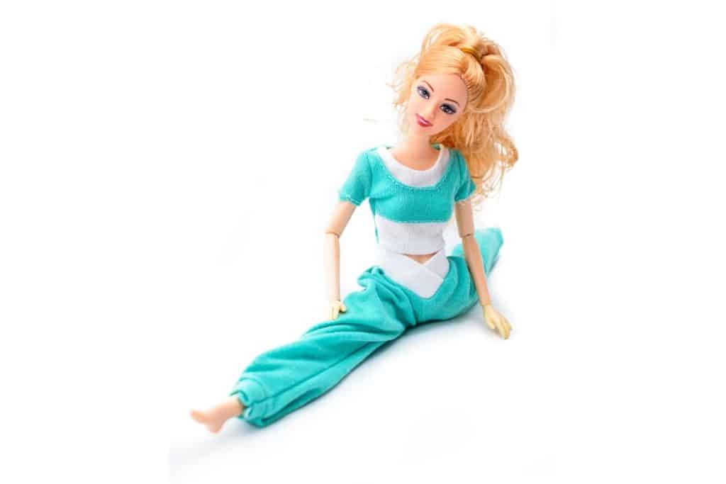 une poupée barbie fait un grand écart en tenue de sport turquoise et blanc. elle a les cheveux en queue de cheval blonds.