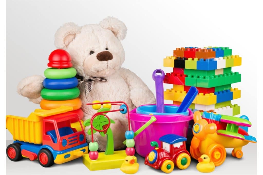 jouets en plastique autour d'un ours en peluche. on voit un camion, des legos, une locomotive, un avion, des seaux, un boulier, des petites canards, un jeu d'empilement